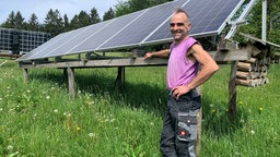 Oliver Junker-Matthes steht stolz vor einigen Solar-Panels auf einer Wiese.