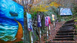 Entlang einer Treppe im Sinneswald werden mehrere Gemälde präsentiert.