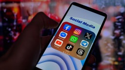 Auf einem Smartphone werden Symbole für verschiedene Social-Media-Apps angezeigt, darunter Facebook, Instagram, X, Threads und TikTok. 