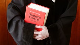 Eine Staatsanwältin in schwarzer Robe hält ein rotes Gesetzbuch in den Armen, Nahaufnahme.