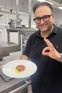 Sternekoch Daniel Georgiev hält einen weißen Teller mit seinem Tomaten-Tartar in der Hand