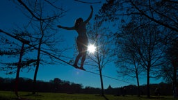 Eine Frau balanciert über eine zwischen zwei Bäumen gespannte Slackline.