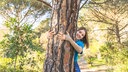 Frau die lachend einen Baum im Wald umarmt