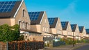 EineReihe neuer Einfamilienhäuser mit Solarpaneelen auf den Dächernvor strahlend blauem Himmel