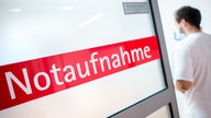 Ein Krankenpfleger steht in einem Krankenhaus neben einer Glastür mit der Aufschrift «Notaufnahme»