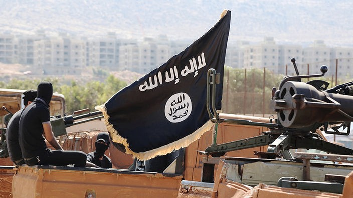Mitglieder der Terrormiliz "Islamischer Staat" posieren auf bewaffneten Fahrzeugen vor einer Häuserfront