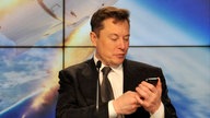 Elon Musk schaut auf sein Mobilphone. 