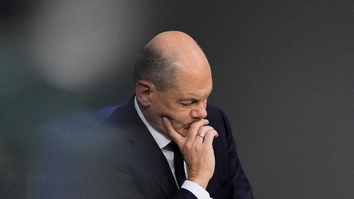 Olaf Scholz stütz seinen Kopf auf seine Hand und nimmt eine nachdenkliche Pose ein.