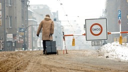 Eine Person zieht einen Koffer durch braunen Schnee neben einem Schild mit der Aufschirft "Smog-Alarn".