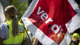 Archivbild: Eine Frau mit gelber Warnweste hält eine Fahne mit dem Logo der Gewerkschaft Verdi.