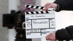 Ein Mitarbeiter eines Filmteams hält eine Filmklappe mit der Aufschrift "Fernsehen".