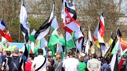 Teilnehmer einer Kundgebung von "Reichsbürgern "stehen mit Fahnen auf dem Versammlungsplatz, 06.04.2024.