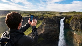 Tourist fotografiert mit Handy den Haifoss-Wasserfal in Island. 