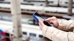 Auf einem Bahnhof wird auf ein Smartphone geschaut. 