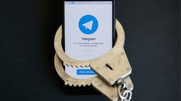 Smartphone mit Telegram-Logo ist mit Handschellen gefesselt.