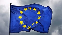 EU-Flagge weht vor dunklem Himmel. 