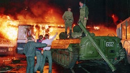 Demonstranten vor einem Panzer, auf dem Soldaten stehen