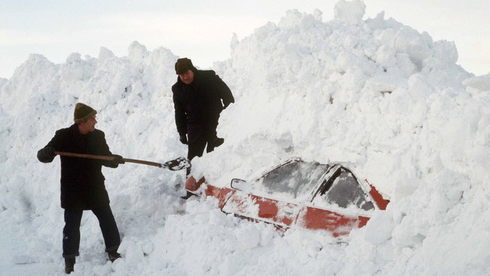 Ein Mann schaufelt ein Auto aus den Schneemassen frei