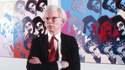 Der  US-amerikanische Popkünstler Andy Warhol vor Bilder aus seiner Serie "Ten Portraits of Jews of the Twentieth Century". 1980