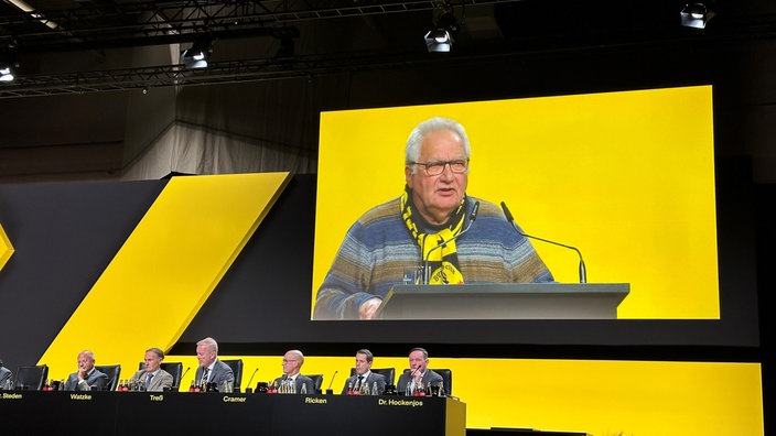 BVB-Mitglied Wilfried Harthan hält auf der Mitgliederversammlung eine Rede. Sein Bild wird auf einer Großleinwand übertragen