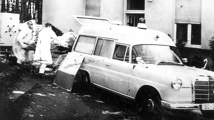 Ein Opfer der Pockenepidemie von 1970 in Meschede wird von Helfern mit Mund-und Atemschutz in einen Krankenwagen verladen