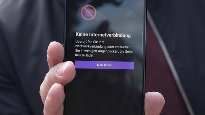 Ein Mann hält ein Handy hoch, welches keine Internetverbindung hat