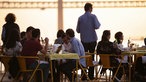 Das Bild zeigt Menschen beim Abendessen auf der Hafenpromenade Ponte Final in Lissabon.