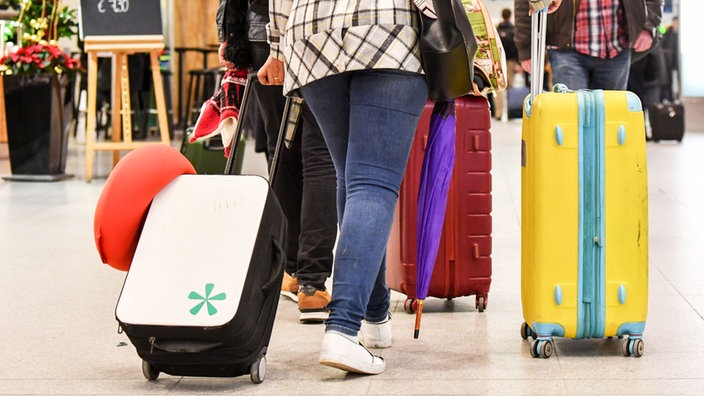 Das Bild zeigt eine Frau, die mehrere Koffer am Flughafen hinter sich her schiebt.