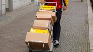 Das Bild zeigt einen Paketzusteller mit einem Stapel Paketen.