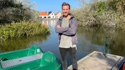 Reporter Daniel Aßmann steht auf einem Steg neben einem Tretboot.