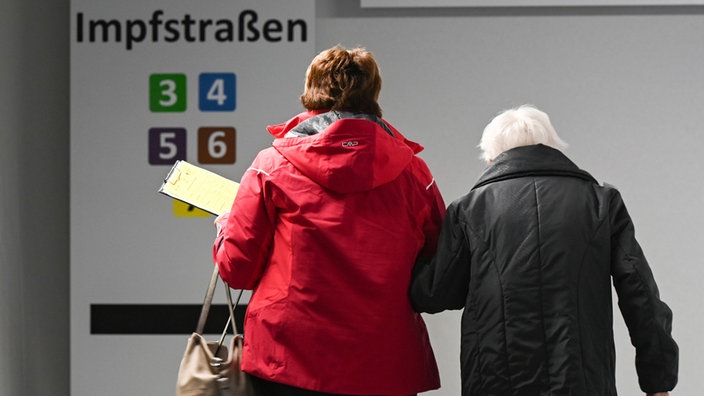 Das Bild zeigt zwei ältere Personen auf dem Weg ins Impfzentrum.