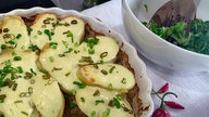 Hackfleisch mit gratinierten Kartoffeln in einer Backform, daneben eine Schüssel Salat