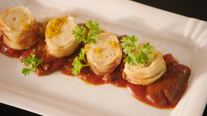 Das Bild zeigt eine Currywurst im Kartoffelnetz mit Zwetschgen-Currysoße.