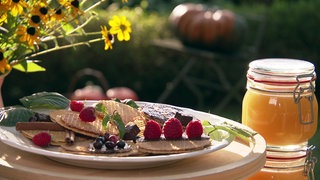 Honigwaffeln mit Beeren auf einem Teller, daneben ein Glas Honig