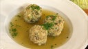 Käseknödel mit Speck in einem tiefen Teller mit Brühe angerichtet