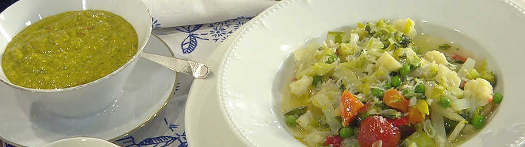 Minestrone in einem Teller angerichtet, daneben Schüsseln mit Basilikumsauce und geriebenem Parmesan