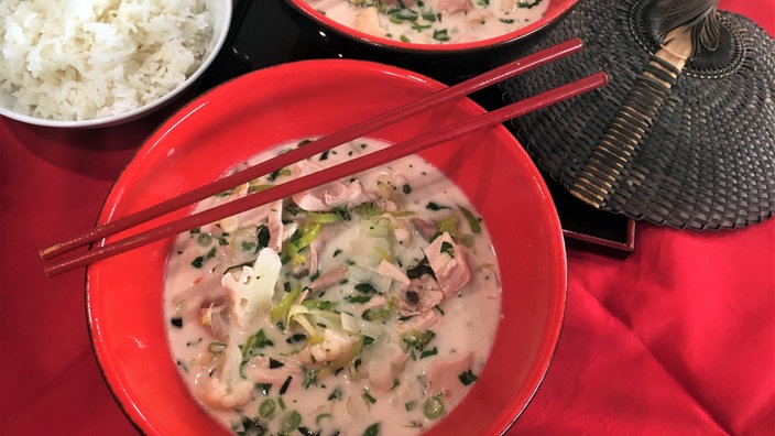 Tom Ka Gai – Thailändische Hühnersuppe in einer Schale angerichtet, darüber liegen zwei rote Essstäbchen