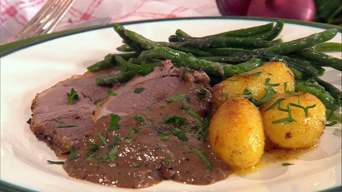 Heidschnuckenbraten mit Wacholdercremesoße, Kartoffeln und grünen Bohnen auf einem Teller angerichtet