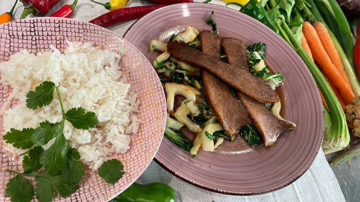 Asiaduftender Brustkern mit Pak Choi auf einem Teller angerichtet, daneben eine Schüssel mit Reis