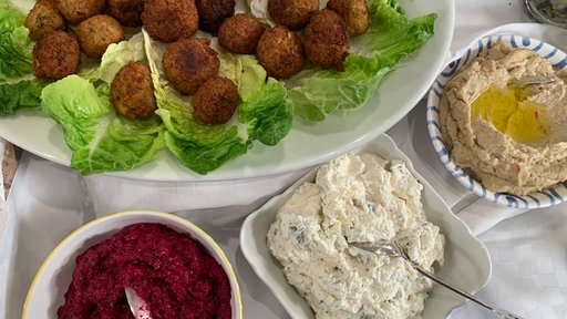 Platte mit kugeligen Falafel auf grünen Salatblättern angerichtet, daneben drei Schüsselchen mit unterschiedlichen Dips