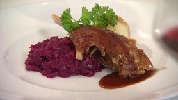 Man sieht eine Portion Martinsgans mit Rotkohl. Serviert auf einem edlen weißen Teller.