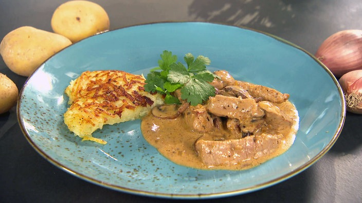 Das schweizerische Gericht "Zürcher Geschnetzeltes" mit Kartoffelrösti auf einem Teller.