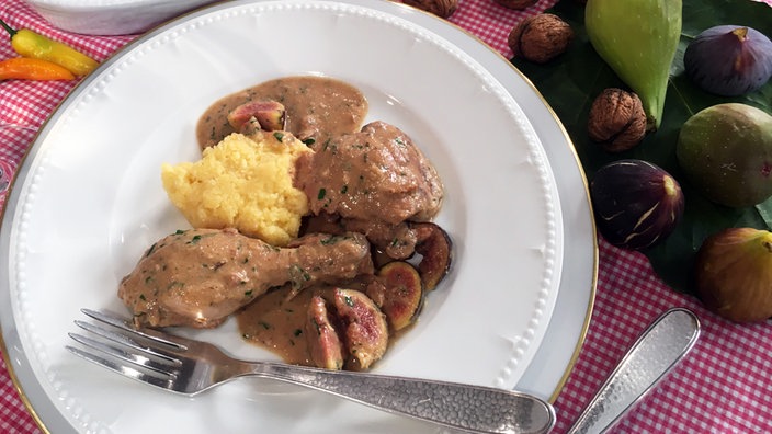 Geschmortes Huhn mit Walnusssoße und Feigen sowie einer Portion Polenta auf einem Teller angerichtet