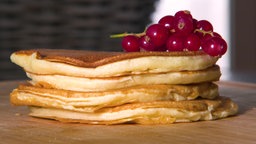 Das Bild zeigt augestappelte Pfannkuchen mit Johannisbeeren serviert.