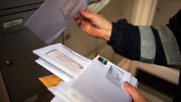 Briefträger mit Briefen vor Briefkasten