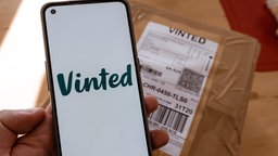 Ein Vinted-Paket wird zum Versand vorbereitet. Dazu ist auch passend die App mit dem Logo geöffnet.